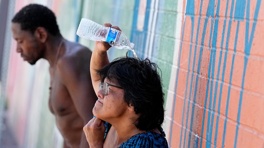 A homeless woman in Phoenix tries to cool down by pouring a bottle of water over her head.