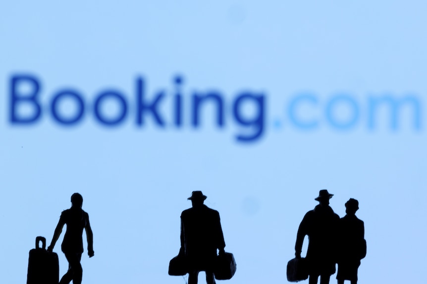 Figurines of travellers walking with bags, in front of a large Booking.com logo in a photographer's illustration.