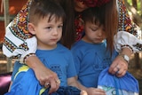 A woman leans over twin boys dressed in matching outfits.