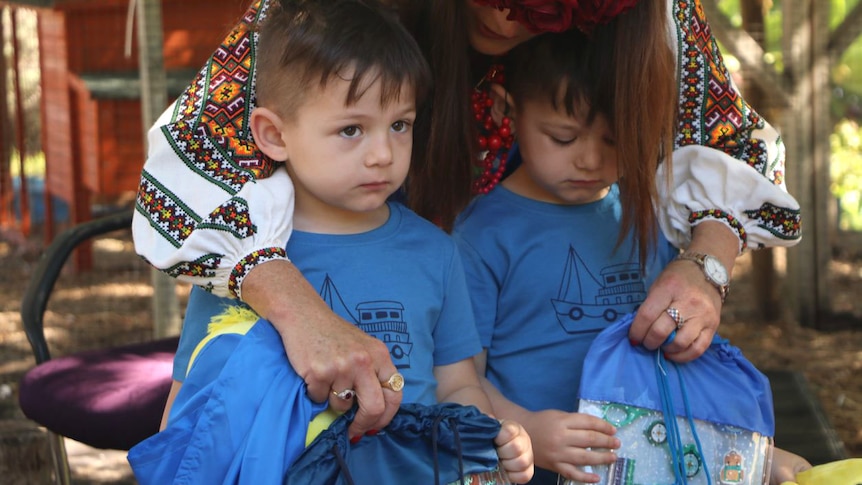 A woman leans over twin boys dressed in matching outfits.