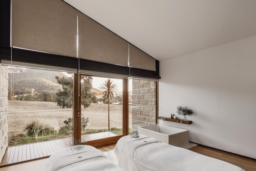two made white beds with running bath in the room, with floor to ceiling windows looking out to mountains
