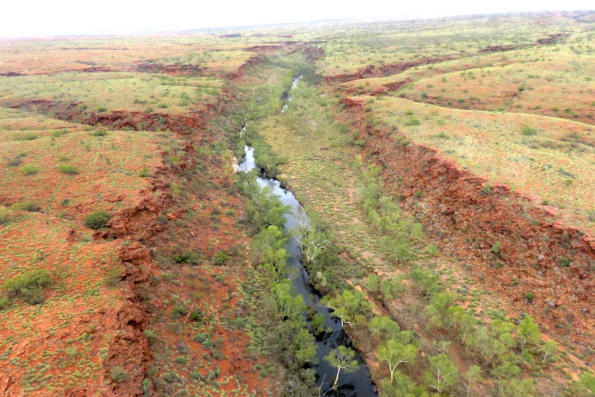 An aerial shot of a large creek with water in it. Countryside is green and red.