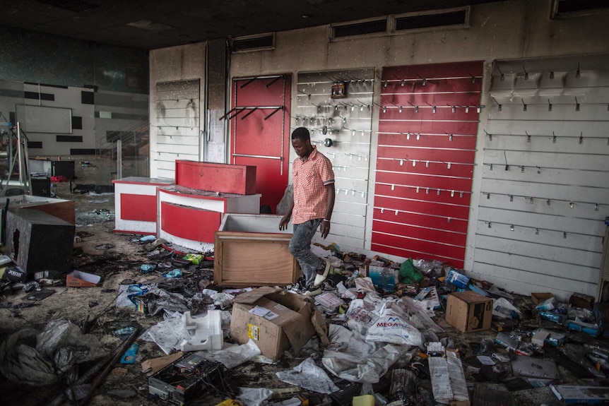An employee walks past debris as he attempts to salvage items from a looted shop in Libreville on September 1, 2016