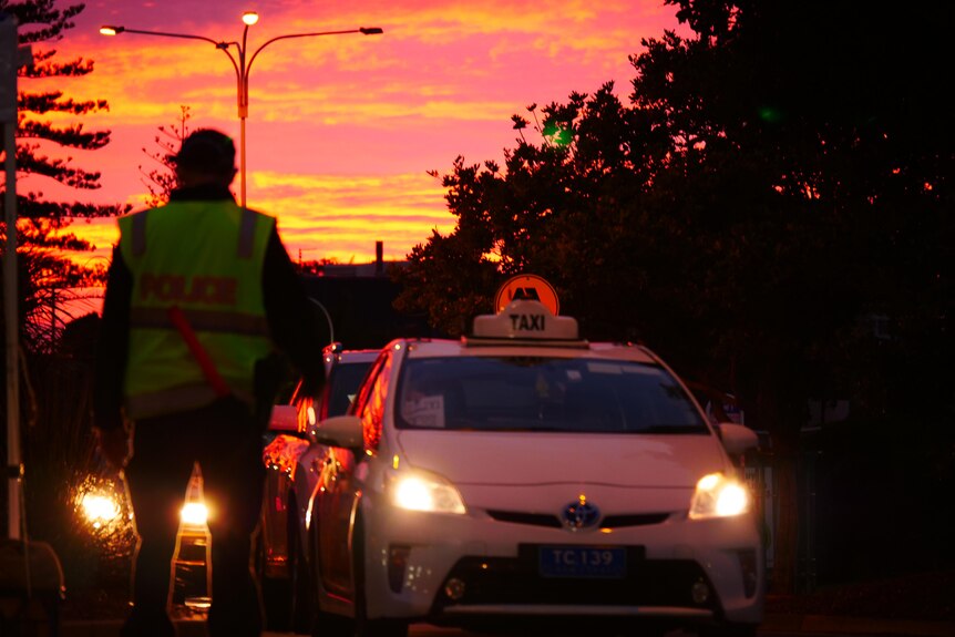 sunrise over a queue of vehicles including a taxi with a police officer in the foreground.