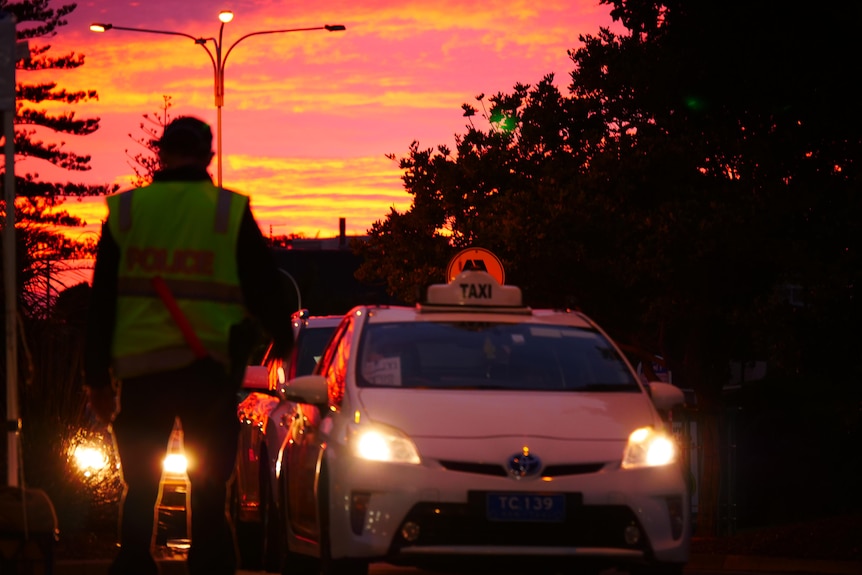 The sun rises with a hypercolour glow over a dark police check point on a Queensland road.