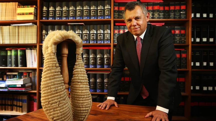 Indigenous lawyer Tony McAvoy SC in his office, with a wig on his desk, surrounded by legal books.