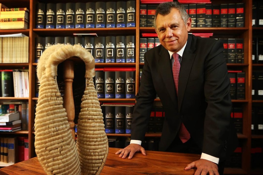 Indigenous lawyer Tony McAvoy SC in his office, with a wig on his desk, surrounded by legal books.