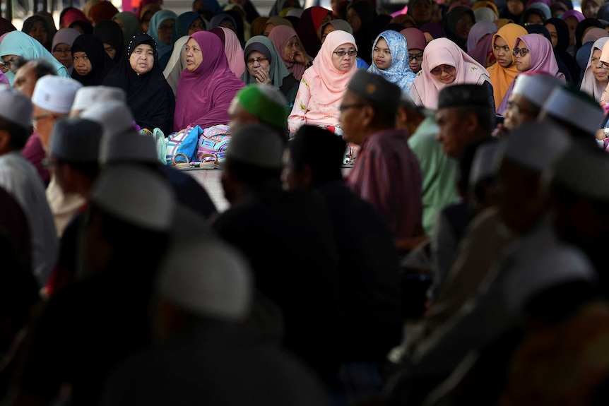 Women in traditional Islamic dress sit together listening to a lecture.