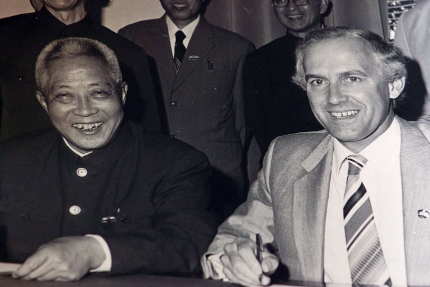 Doug Lowe, sits at a desk, smiling, while in China in 1980.
