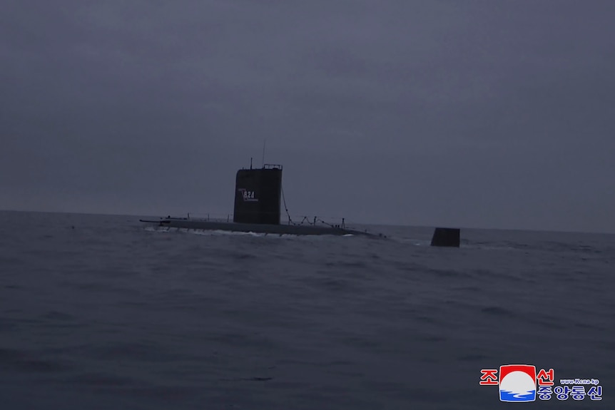 A DPRK submarine sits just above the waterline in a calm sea. 