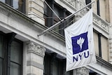 A purple and white NYU flag hangs from a brownstone building in New York City.