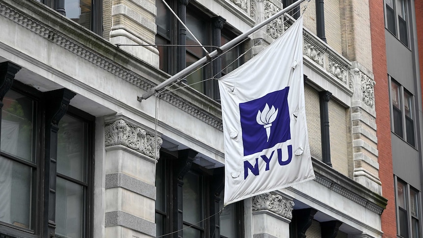 A purple and white NYU flag hangs from a brownstone building in New York City.