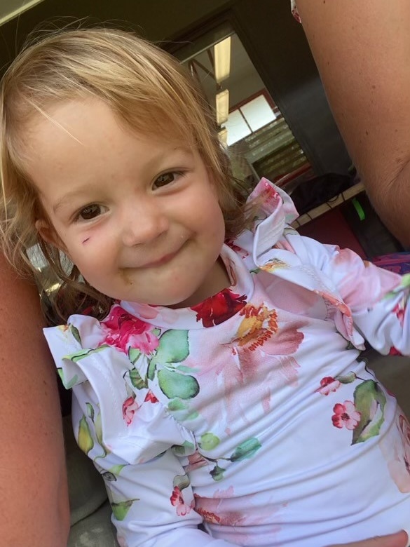 A cute blonde-haired toddler smiles at the camera.