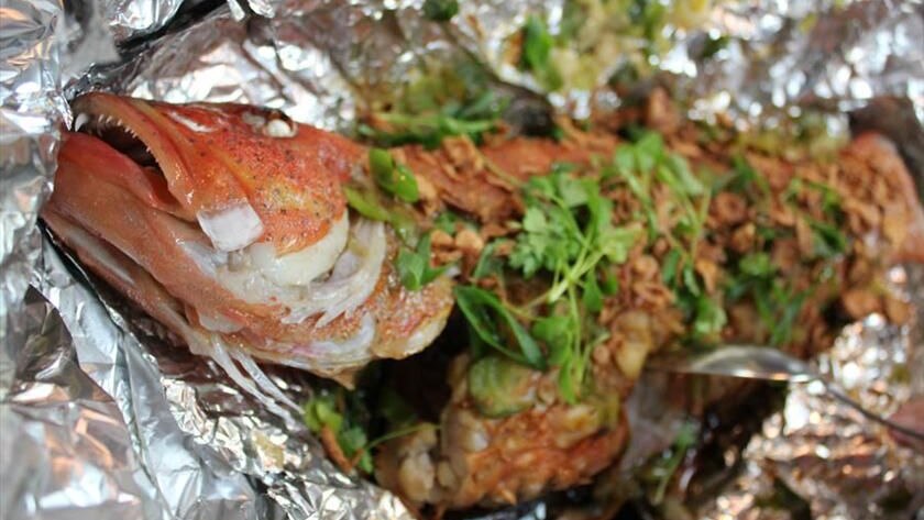 A baked fish with herbs on a crumpled piece of aluminium foil.