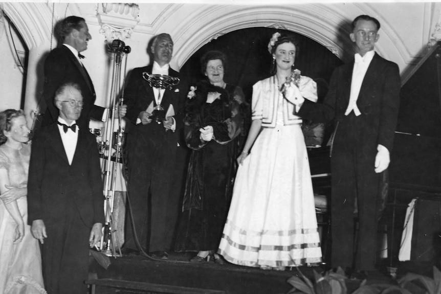Black and white photo of couple in evening wear presenting a trophy to a man and a woman in evening wear.