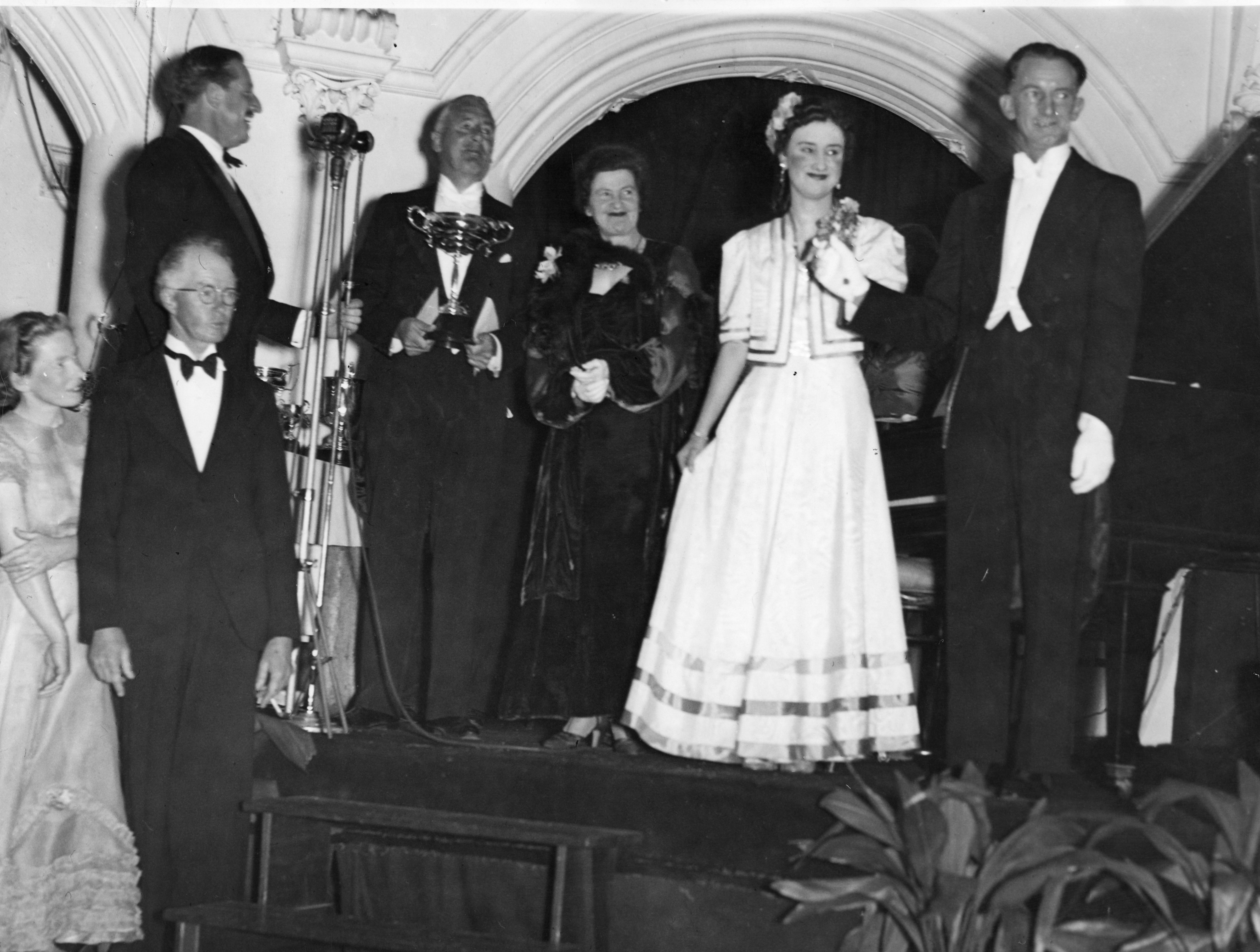 Black and white photo of couple in evening wear presenting a trophy to a man and a woman in evening wear.
