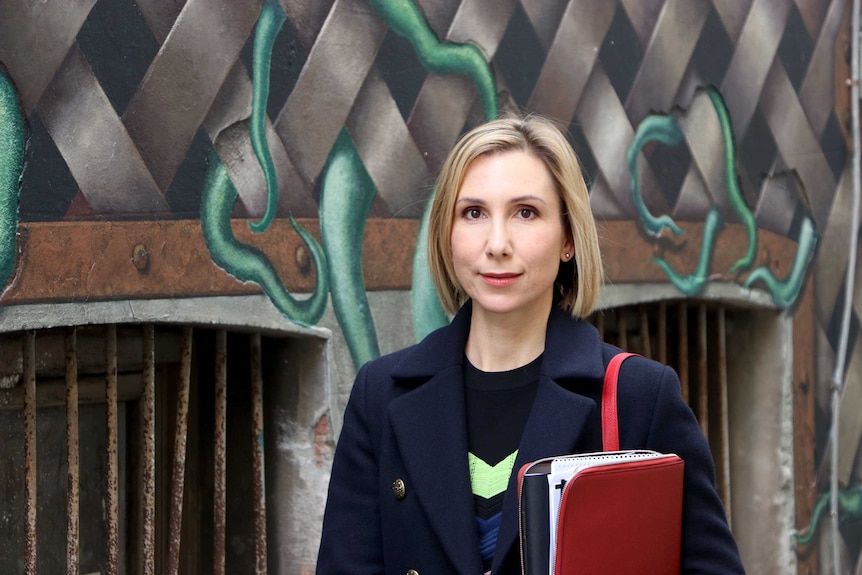 A woman holding an organiser folder standing in front of a wall mural.