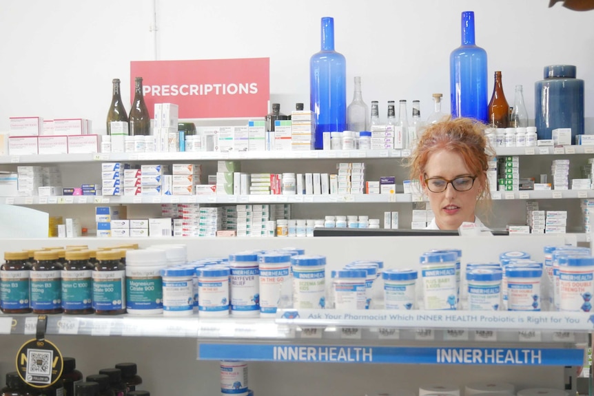 Pharmacist working behind shelves full of products with antique bottles behind her.