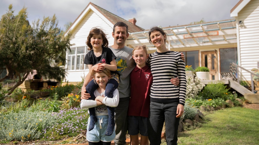 A family of five standing in front of a house, smiling.