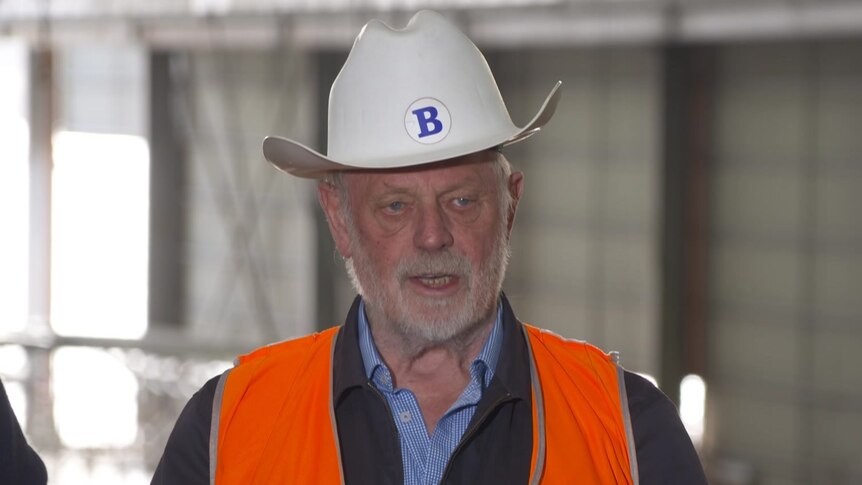 Bob Clifford is an older man with white hair and wearing a hard hat and hi vis orange vest.