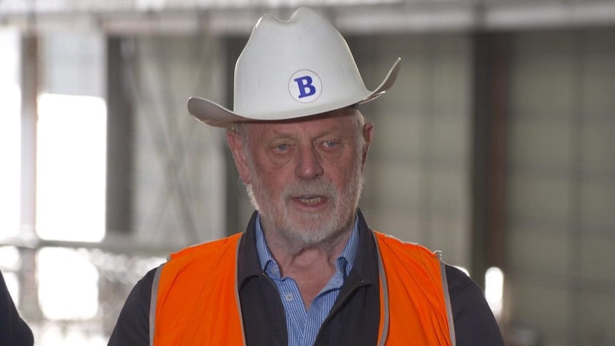 Bob Clifford is an older man with white hair and wearing a hard hat and hi vis orange vest.