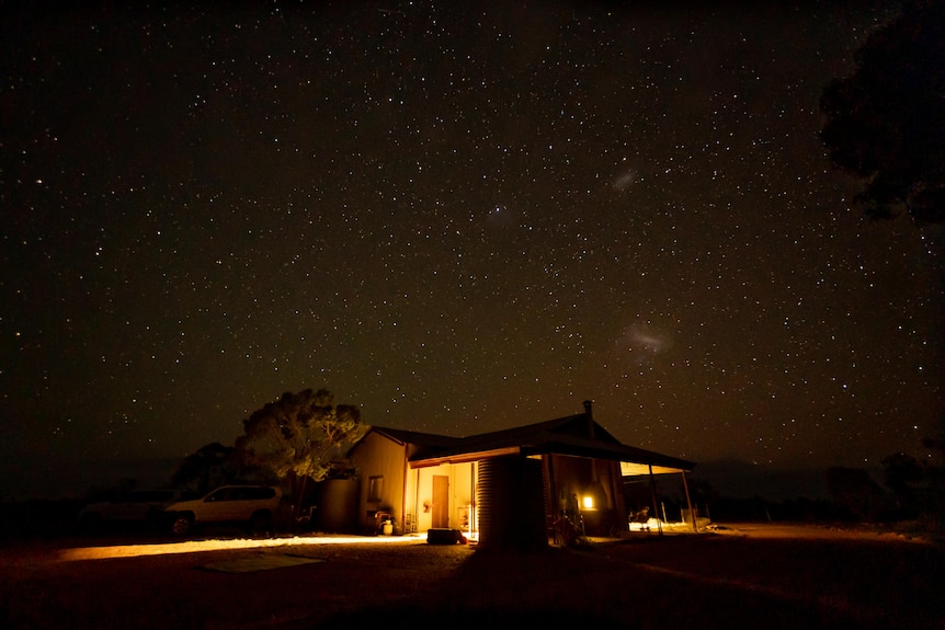 A house pictured at night with warm light from within and stars above