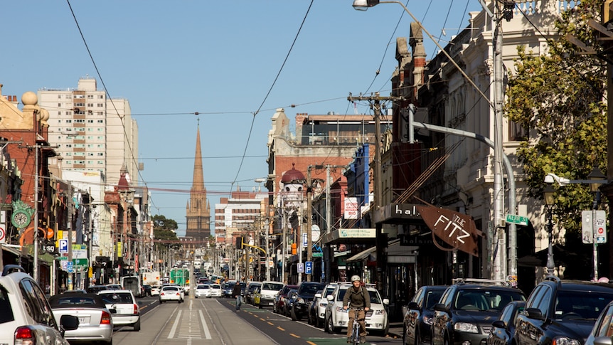 Cars and a bike on a road lined with cafes and bars.