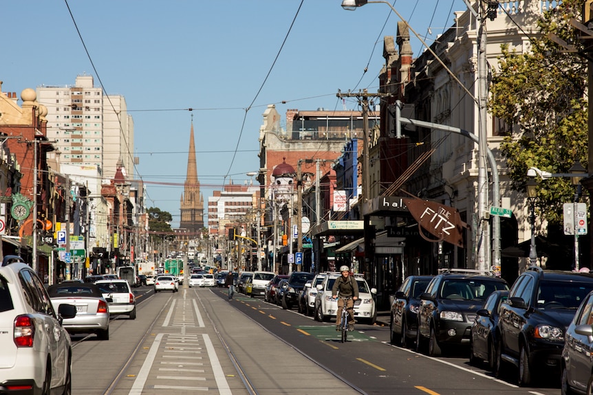 Cars and a bike on a road lined with cafes and bars.