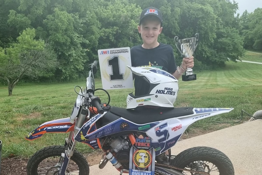 A young boy stands with his trophy and number one plaque 