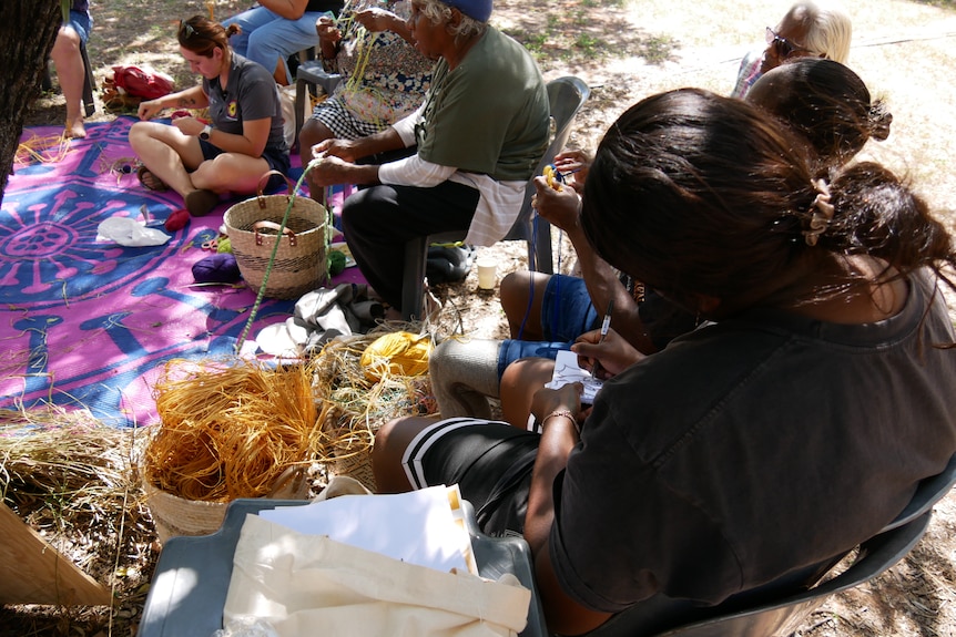 Women sit around holding yarn as they weave colourful baskets