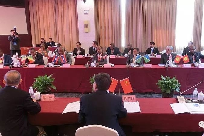 A group of representatives sit around conference meeting tables alongside their country flags.  