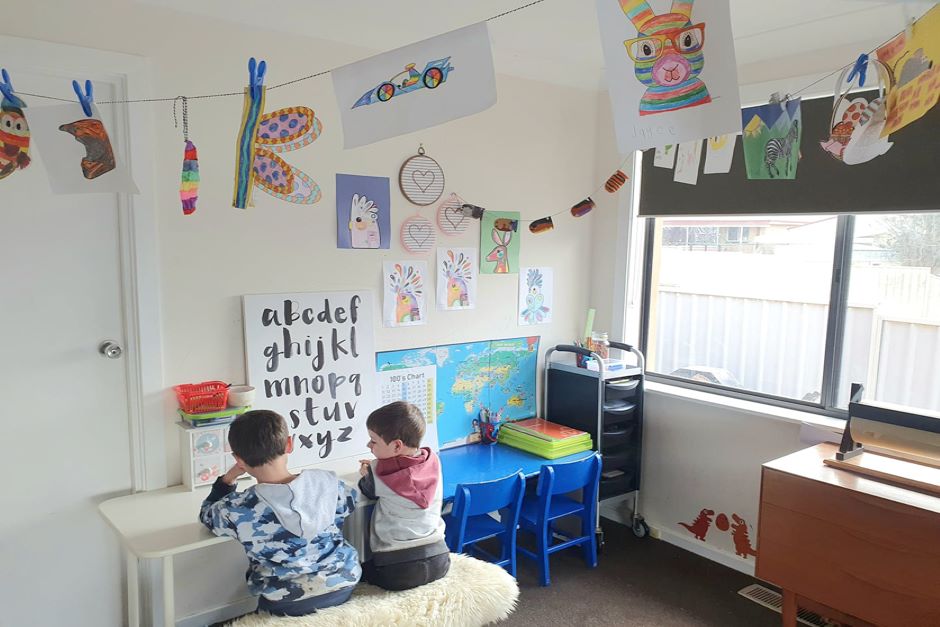 Two children sit at desk at home surrounded by artwork and stationery