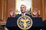 A white man in a suit stands and gestures at a us government podium 