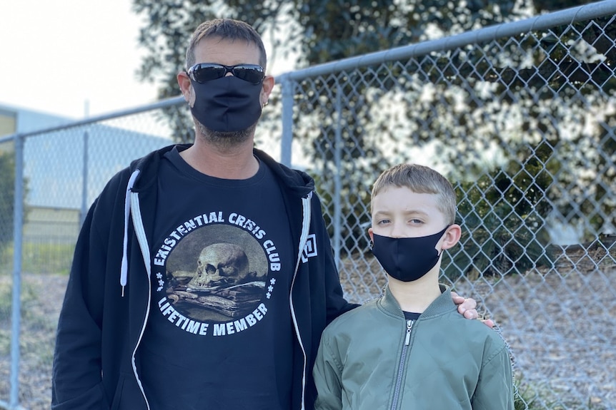 A man and boy stand together outside each wearing a black face mask