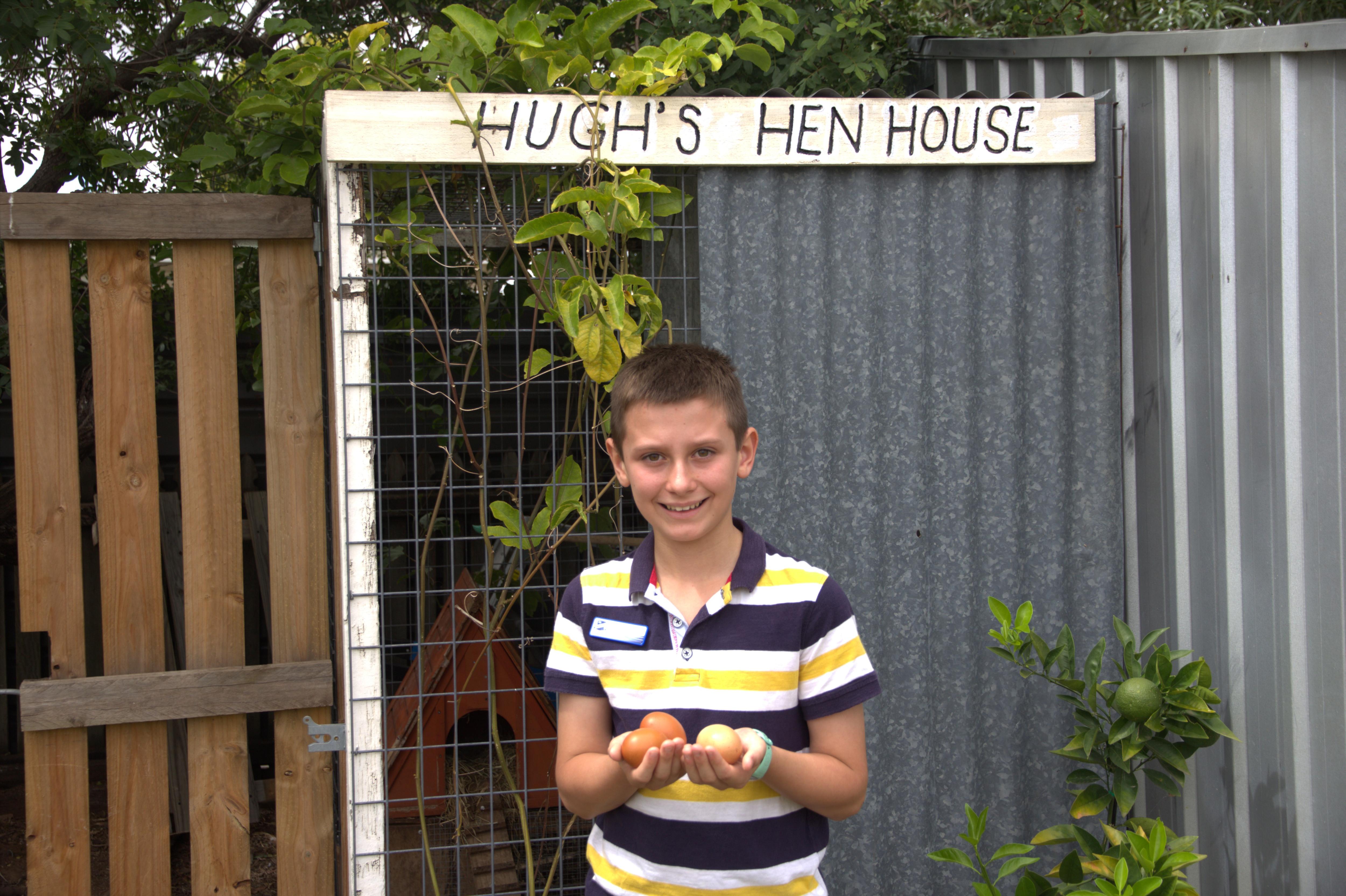 Un niño sostiene huevos frente a un cartel que dice "El gallinero de Hugh"