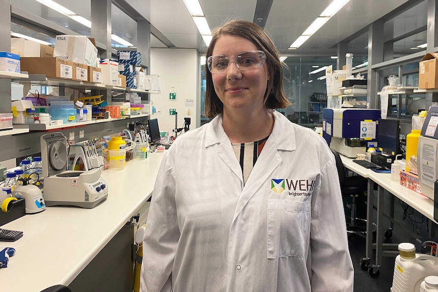 A woman in a laboratory wears a lab coat and protective glasses.