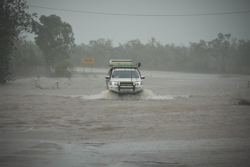 A car driving through floodwater in Broome, with water splashing.
