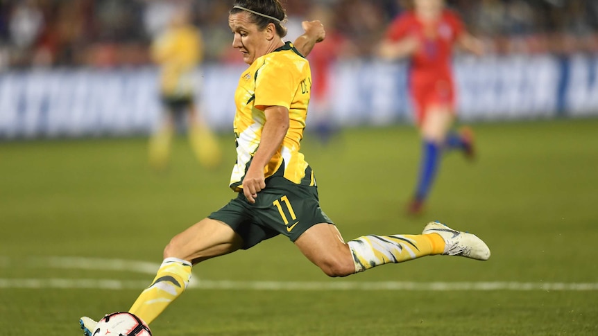 Lisa De Vanna prepares to strike a white soccer ball with her left foot wearing a yellow shirt