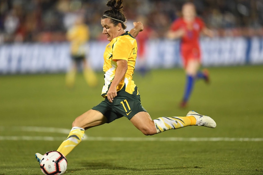 Lisa De Vanna prepares to strike a white soccer ball with her left foot wearing a yellow shirt