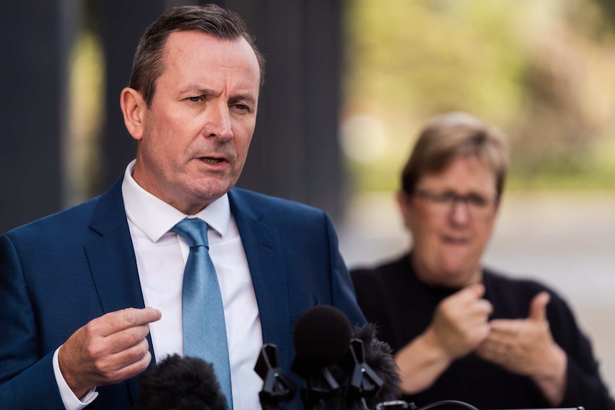 Mr McGowan speaks at a podium, a sign language interpreter stands behind him.