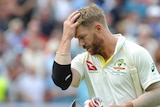 Australia batsman David Warner brushes his hair back as he walks off the ground with his head down.