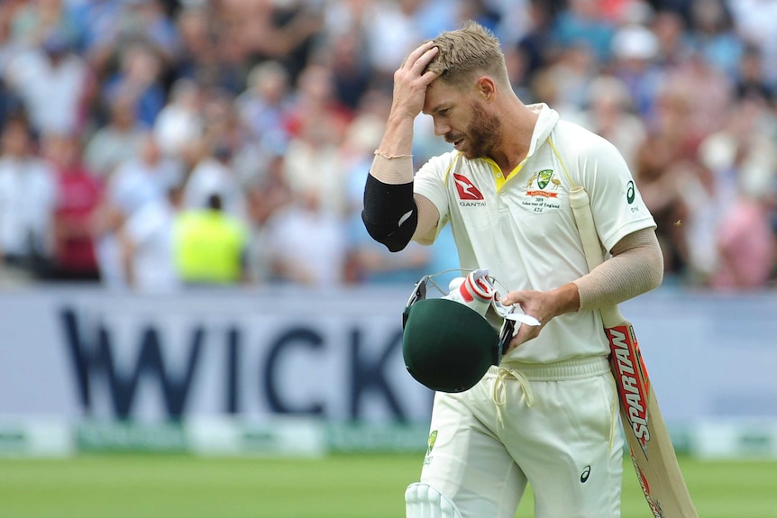 Australia batsman David Warner brushes his hair back as he walks off the ground with his head down.