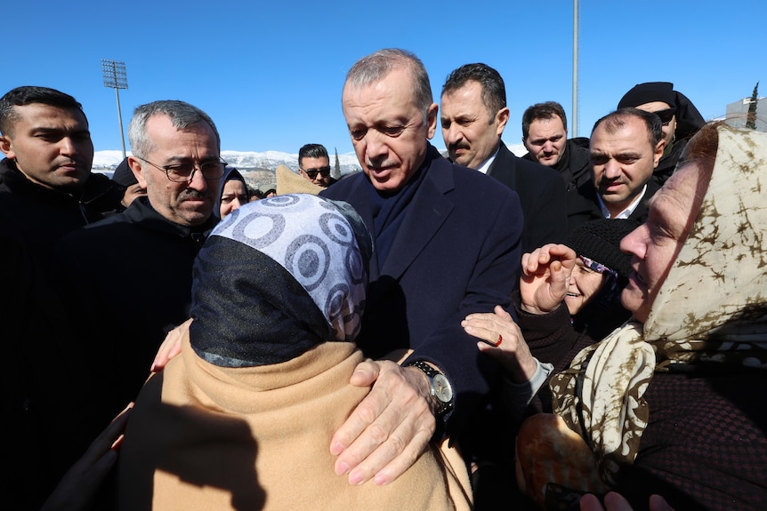 Turkish president places hand on shoulder of elderly woman during tour of quake affected areas.