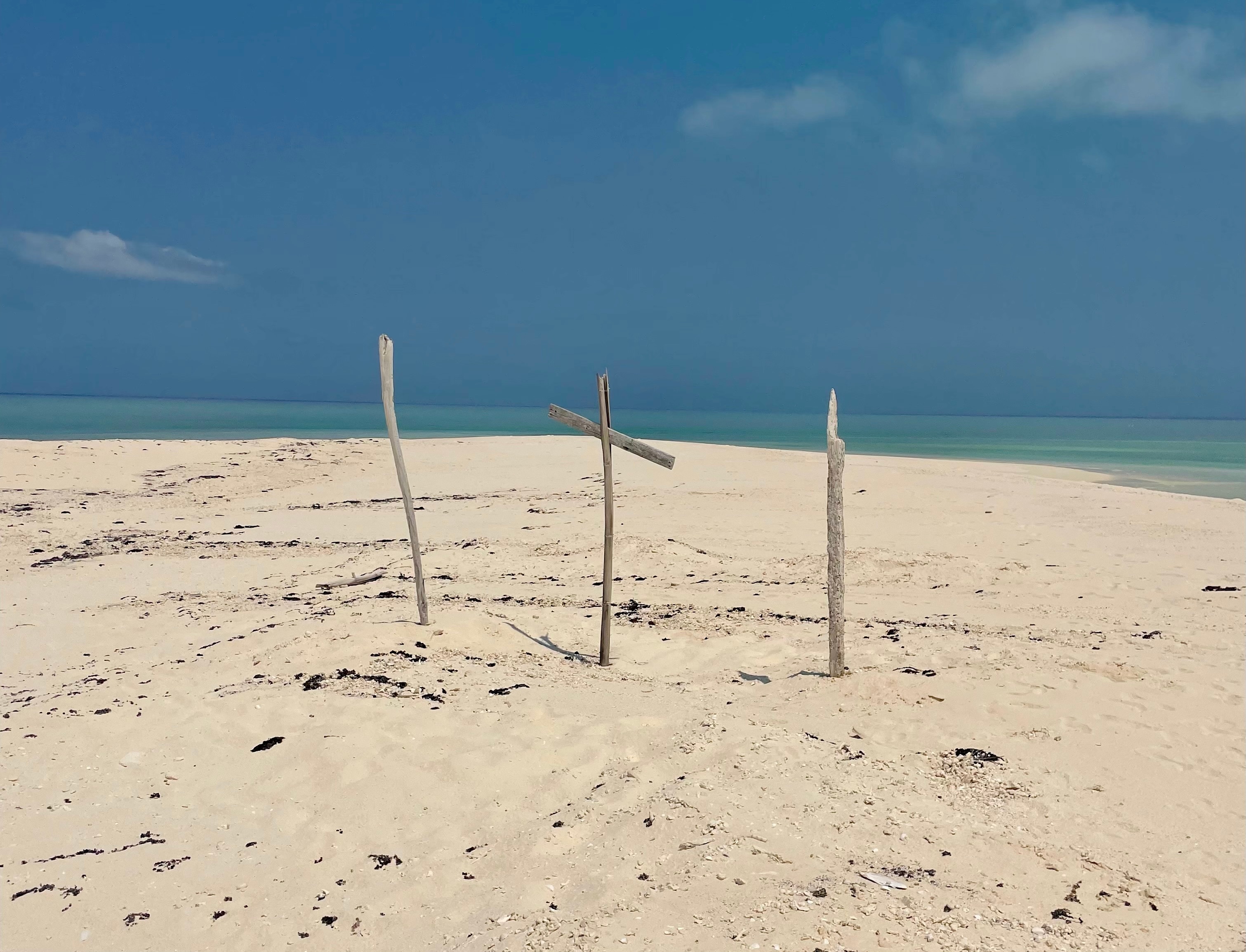 Sticks and a makeshift cross stick out of the sand on a beach
