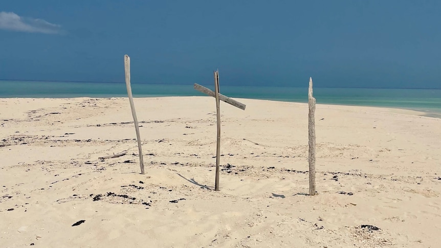 Sticks and a makeshift cross stick out of the sand on a beach