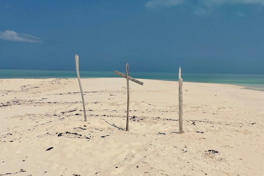 Sticks and a makeshift cross stick out of the sand on a beach