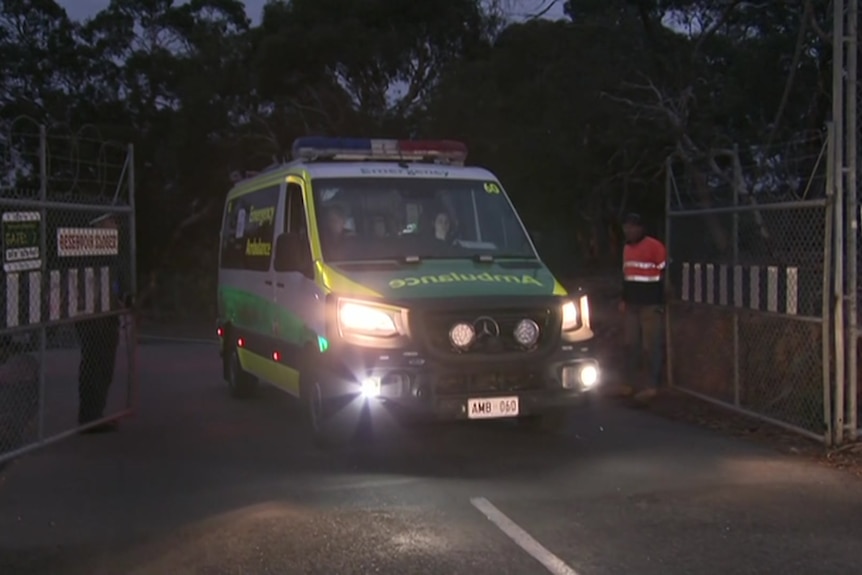 An ambulance leaves through a wire gate with its lights on from the Barossa Reservoir