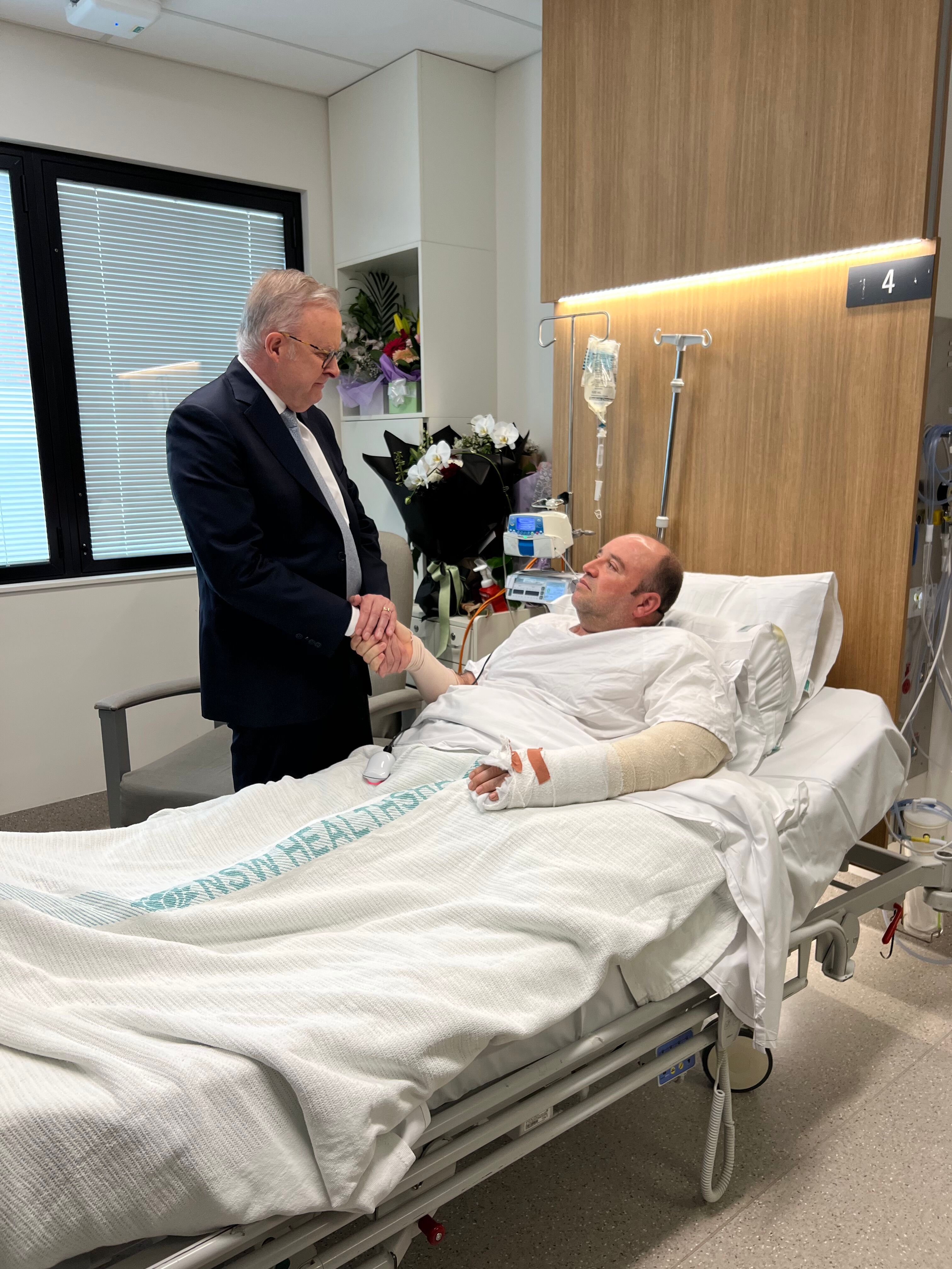 The prime minister shakes Ahmed Al Ahmed's hand in hospital bed