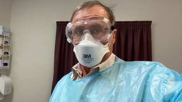 A doctor wearing full PPE including goggles, blue gown and mask.