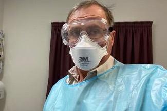 A doctor wearing full PPE including goggles, blue gown and mask.